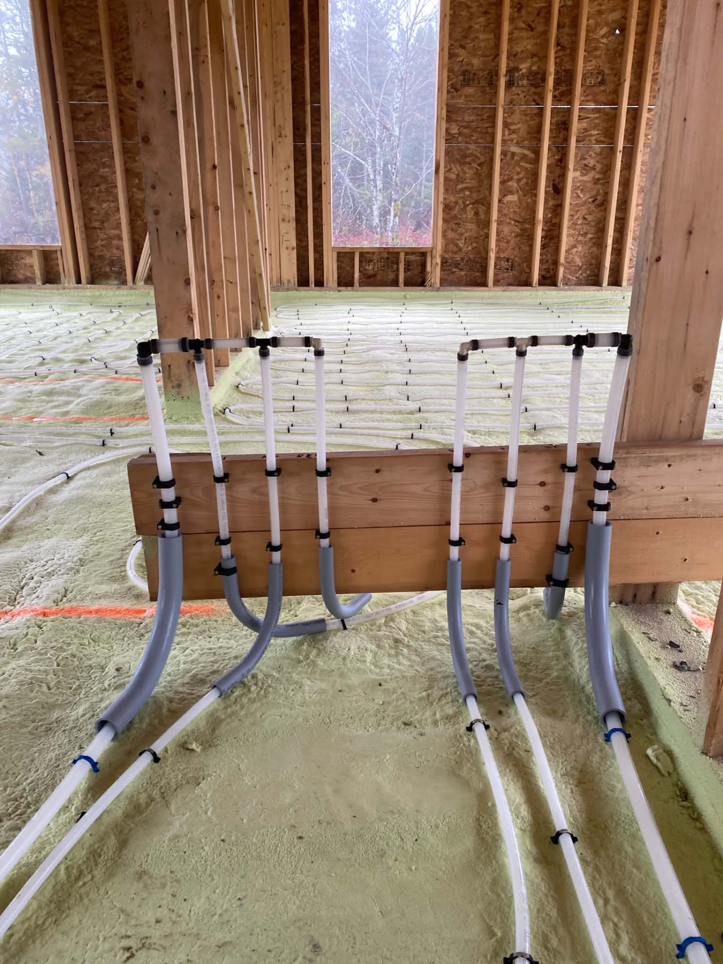 White in-floor heating loops and rough-in stub-outs secured to wooden framing in a house under construction